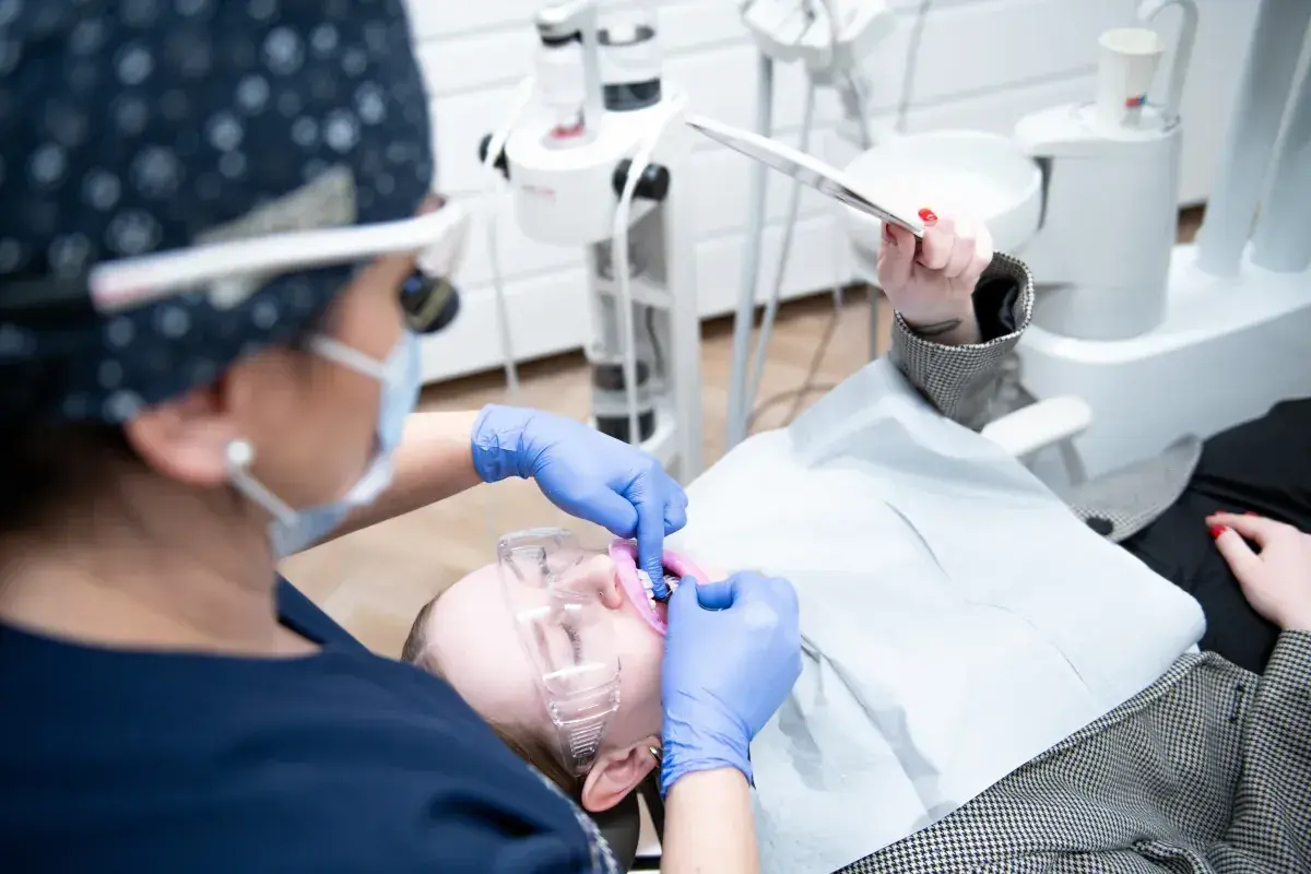 Dentystka w rękawiczkach wykonuje nitkowanie zębów u pacjentki w okularach ochronnych.